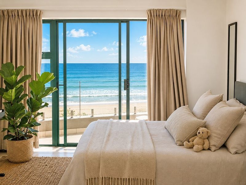 A bright bedroom featuring large sliding glass doors that open onto a balcony with direct ocean views.