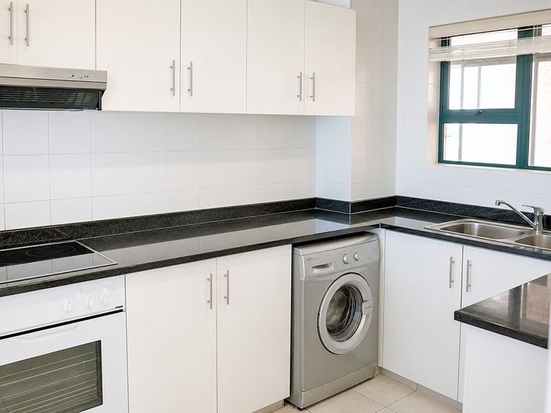 A clean, modern kitchen featuring white cabinetry, dark granite countertops, built-in oven, electric hob, and integrated laundry appliance space.