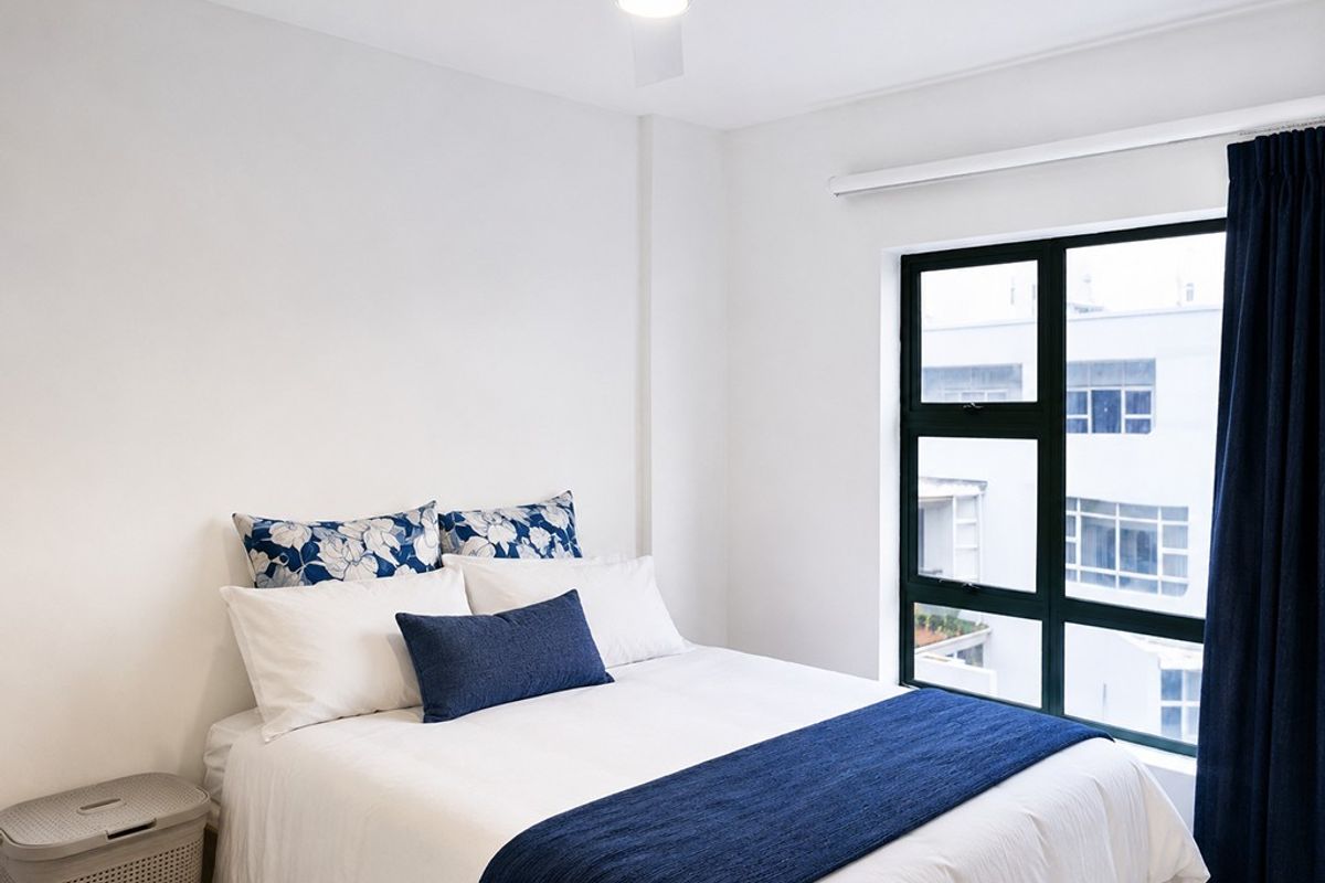 A bright and well-maintained bedroom featuring a ceiling fan and large aluminium-framed windows providing natural light.
