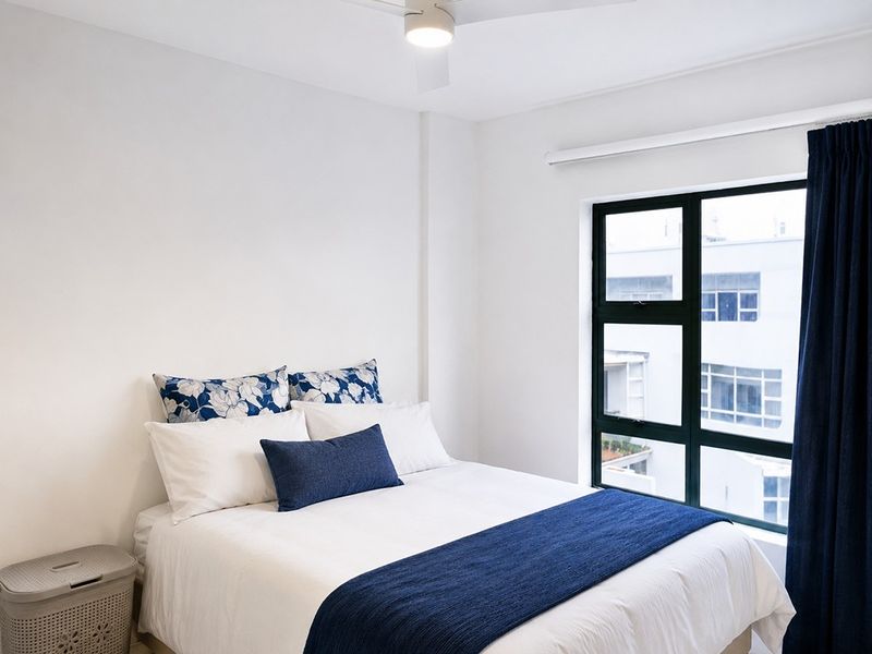 A bright and well-maintained bedroom featuring a ceiling fan and large aluminium-framed windows providing natural light.