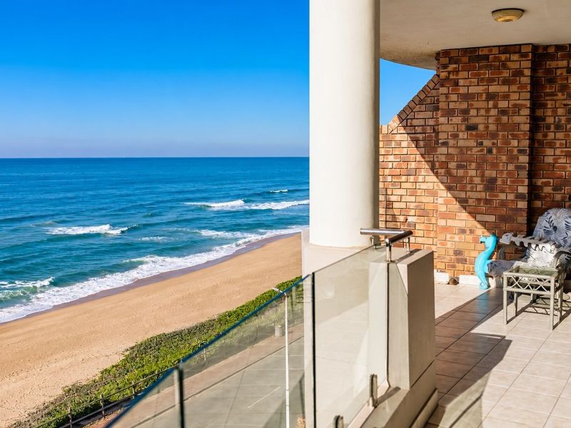 Spacious balcony featuring a glass balustrade and brick wall, offering panoramic ocean and beach views.