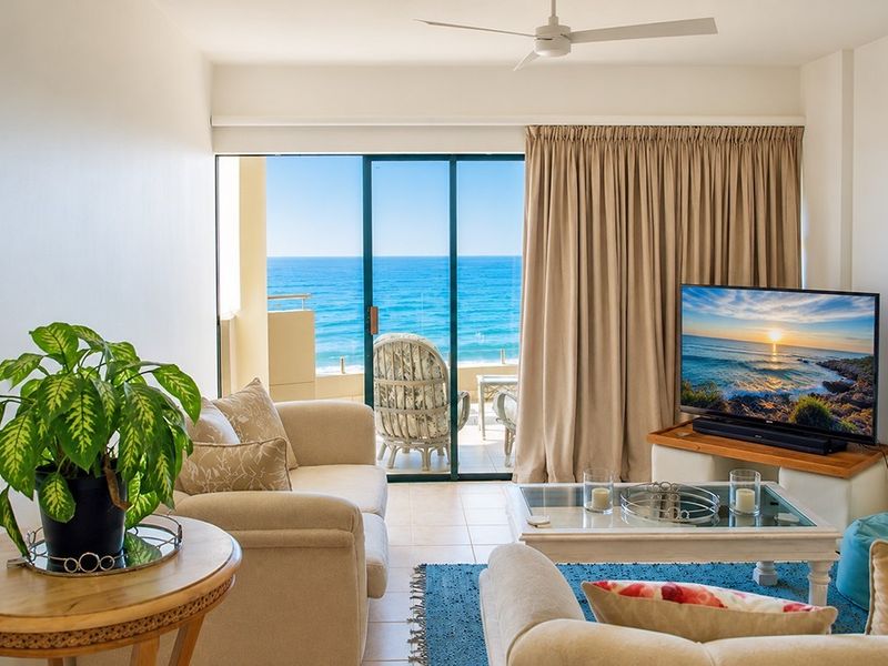 A bright living room featuring tiled flooring, a ceiling fan, and large sliding glass doors that open to a balcony with ocean views.