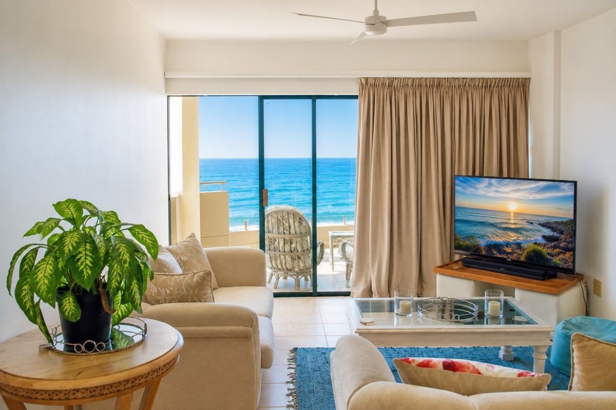 A bright living room featuring tiled flooring, a ceiling fan, and large sliding glass doors that open to a balcony with ocean views.