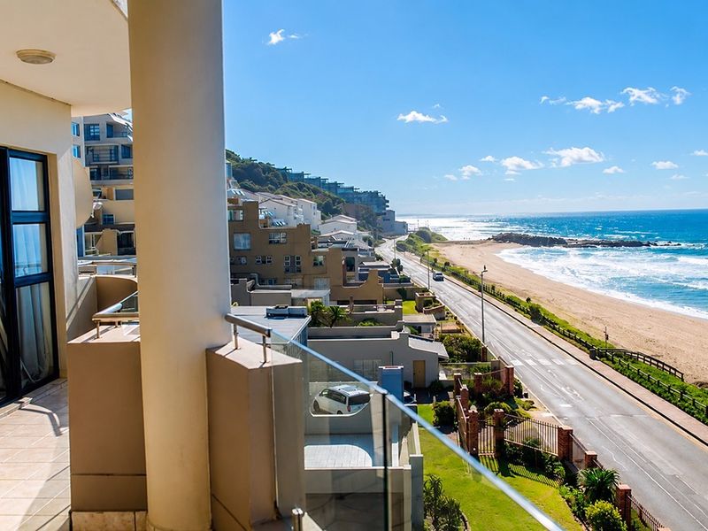 A spacious balcony featuring a modern glass balustrade and tiled flooring, offering expansive coastal and ocean views.