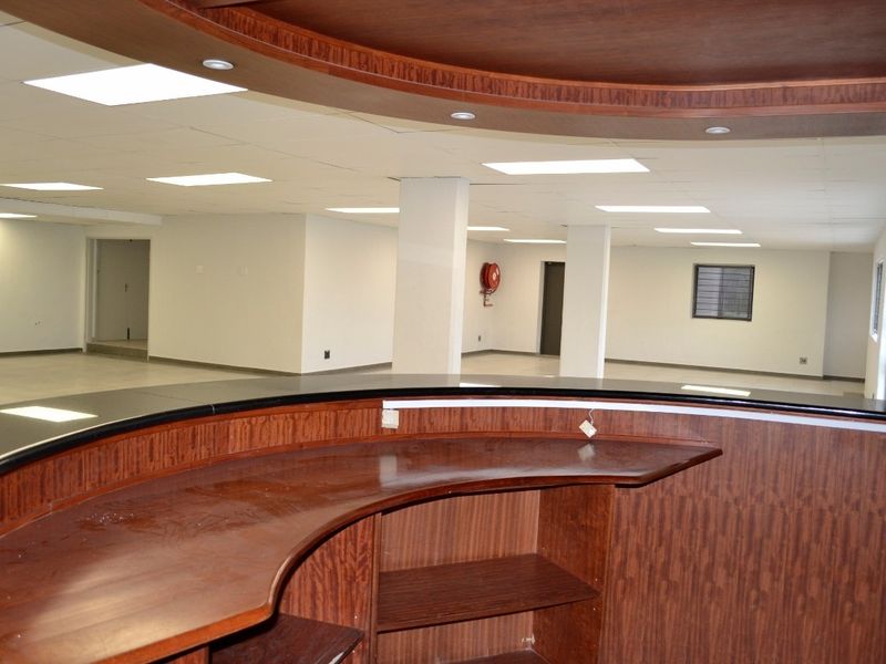 Spacious open-plan commercial office area featuring a built-in reception counter, suspended ceilings with recessed lighting, and structural support columns.