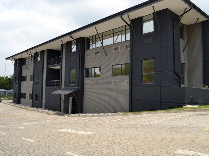 Modern commercial building exterior featuring a dark brick facade, metal roofing, and integrated parking area with paved surfaces.
