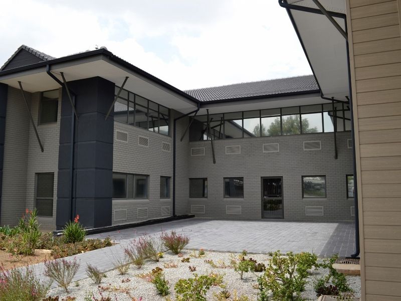 A modern commercial building exterior featuring a paved courtyard, grey brick facade, and clean architectural lines.