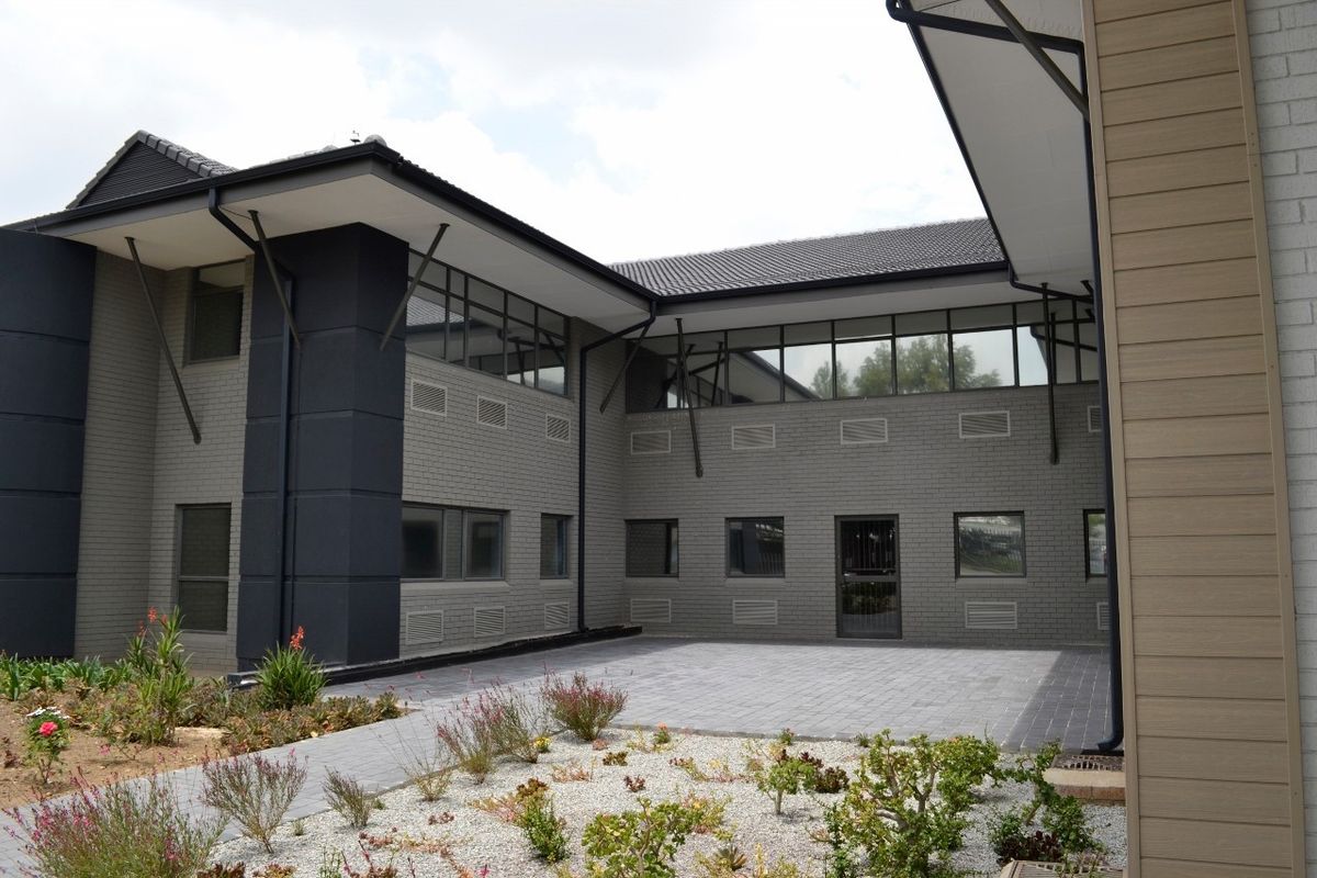 A modern commercial building exterior featuring a paved courtyard, grey brick facade, and clean architectural lines.