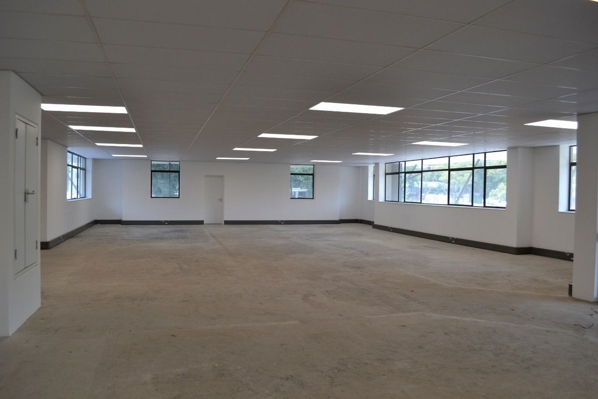 A spacious, open-plan commercial office area featuring a suspended ceiling, recessed lighting, and large windows providing ample natural light.