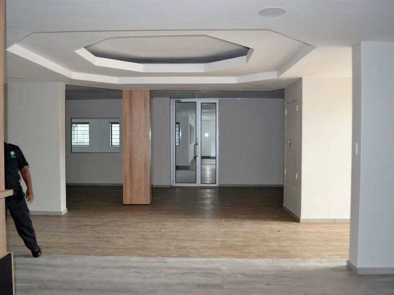 Spacious open-plan commercial area featuring modern wood-look flooring, a decorative recessed ceiling, and a glass-panelled entrance door.