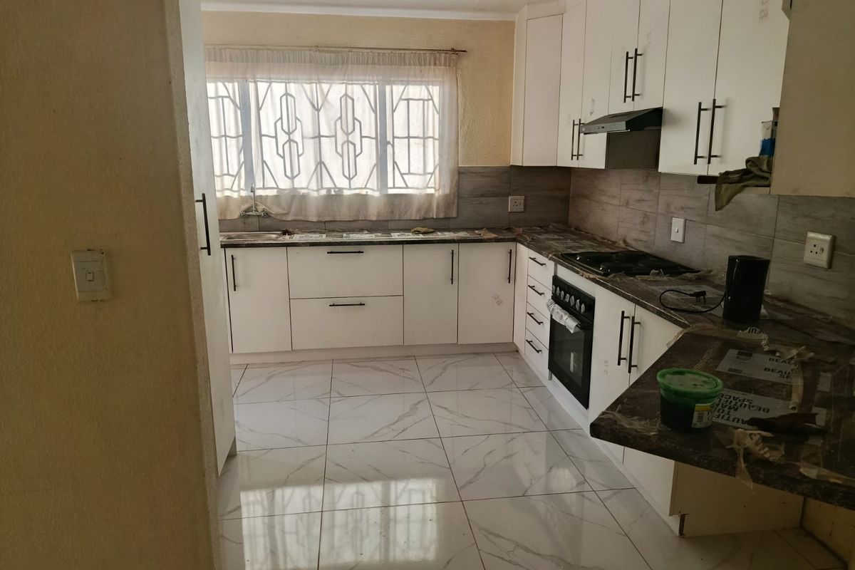 A functional kitchen featuring white cabinetry, built-in oven with gas hob, extractor fan, and modern marble-look porcelain floor tiles.