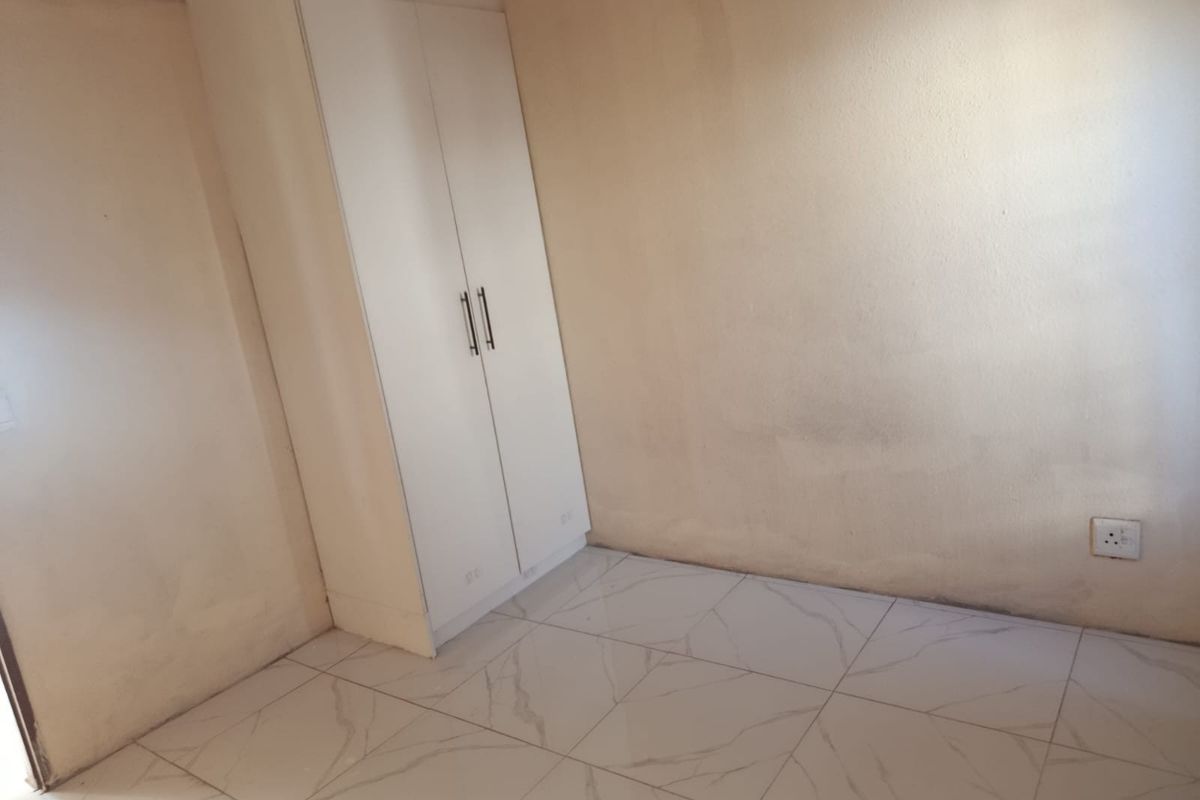 An empty bedroom featuring white tiled flooring and a built-in wardrobe, requiring minor cosmetic updates to the walls.