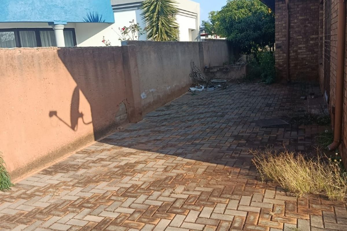 A rear exterior area featuring brick paving, a boundary wall, and brick building facade, requiring maintenance and cleaning.