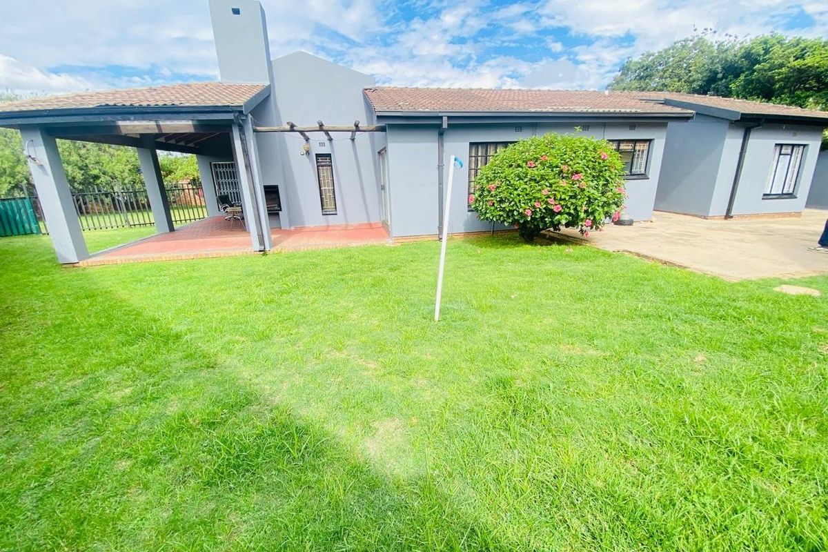 Rear view of the house featuring a covered patio with a built-in braai, overlooking a well-maintained garden and lawn area.