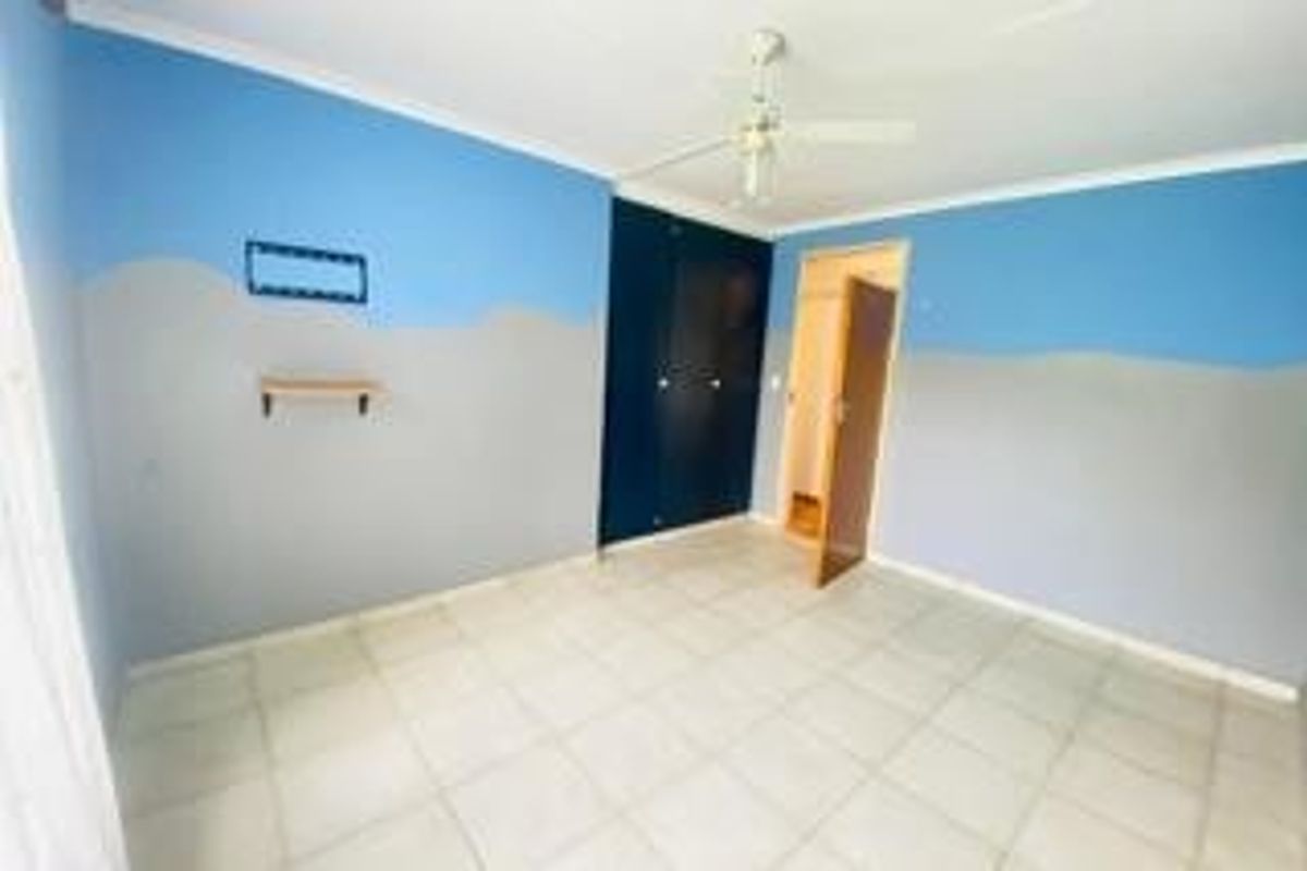 A vacant bedroom featuring tiled flooring, built-in cupboards, and a ceiling fan, finished with a two-tone blue and grey wall paint scheme.