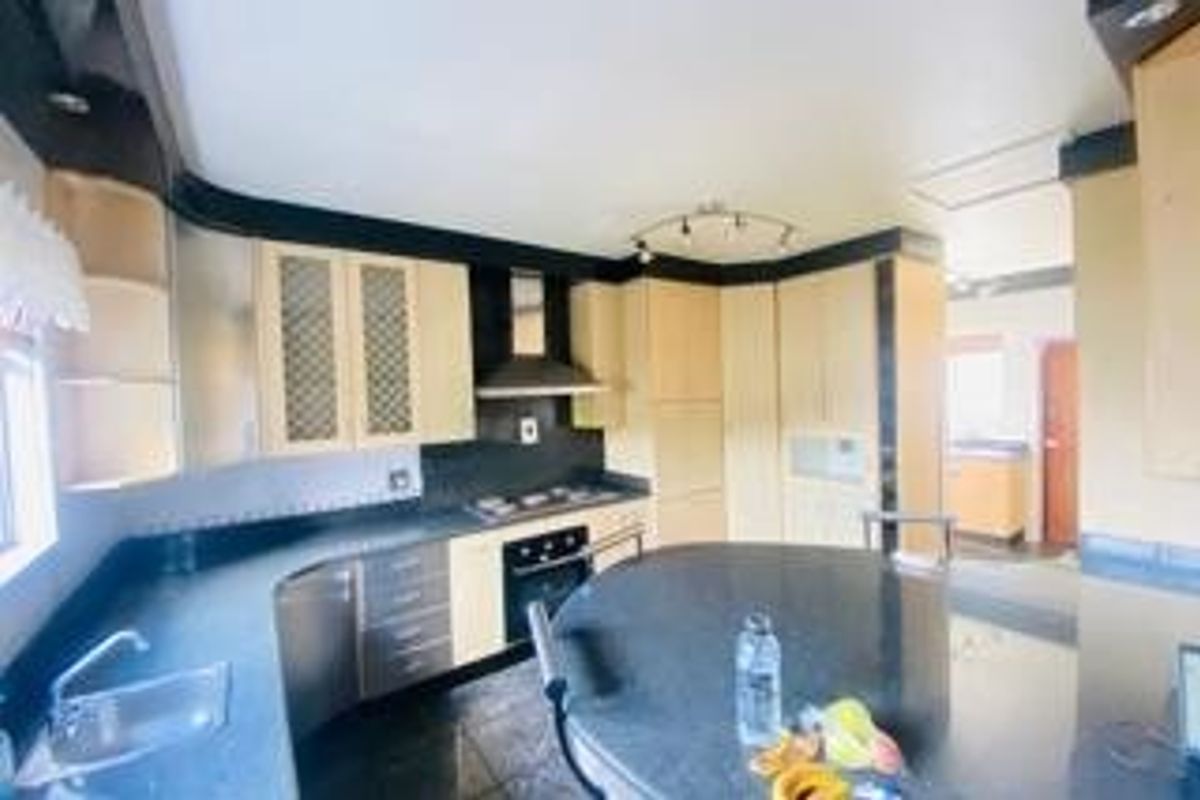A functional kitchen featuring light wood cabinetry, dark stone countertops, a central island, and integrated appliances including an oven and extractor fan.