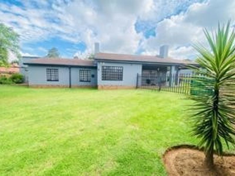 Rear view of the house featuring a spacious lawn, covered patio area, and secure metal fencing.