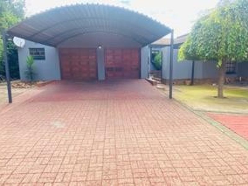 Front exterior view featuring a paved driveway, a covered carport, and a double garage with wooden doors.