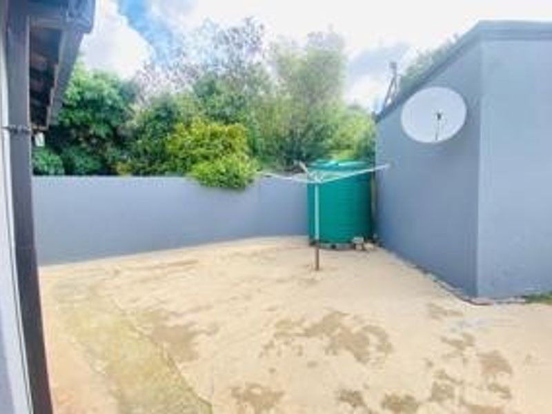 A rear exterior area featuring a concrete paved courtyard, boundary walls, and a water storage tank.
