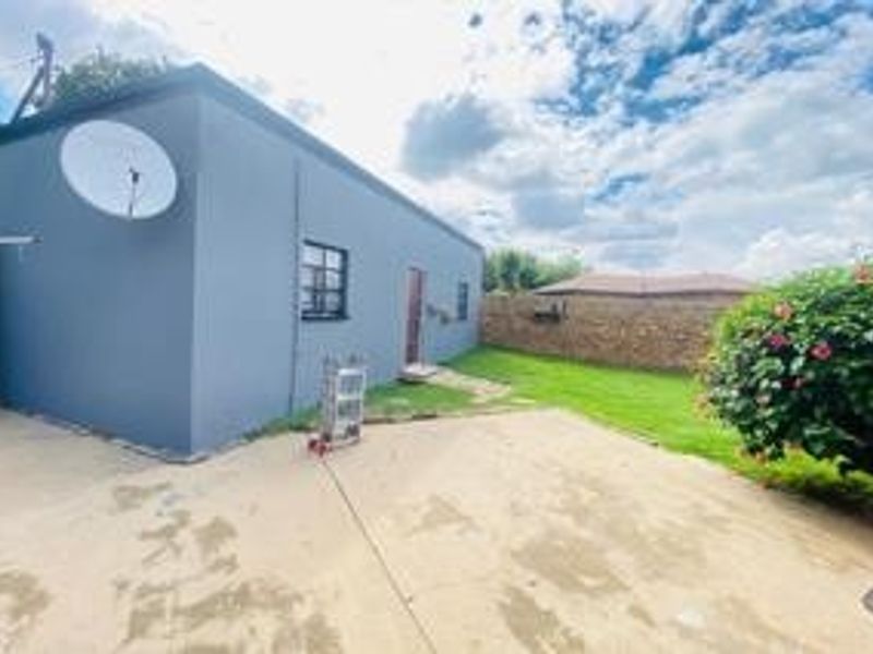 Rear exterior view of the property featuring a concrete patio area, a stone boundary wall, and a satellite dish mounted on the side wall.