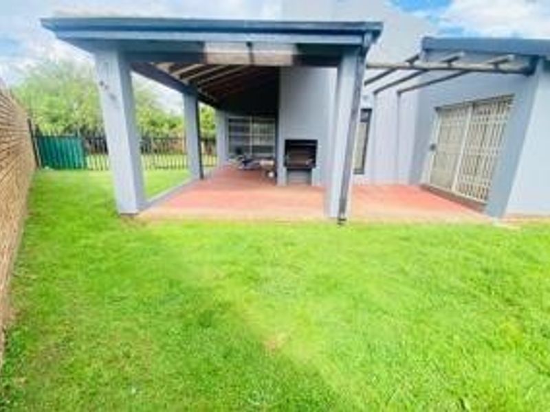A covered patio area featuring a built-in braai, brick paving, and direct access to the garden through sliding doors.