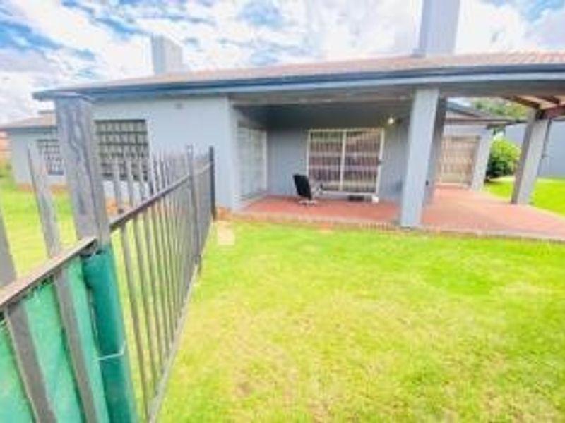 Rear view of the property featuring a covered patio area, sliding glass doors, and a private lawn enclosed by metal security fencing.