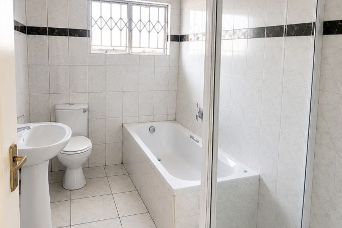 A functional bathroom featuring a pedestal basin, toilet, bathtub, and a separate shower enclosure with tiled finishes throughout.