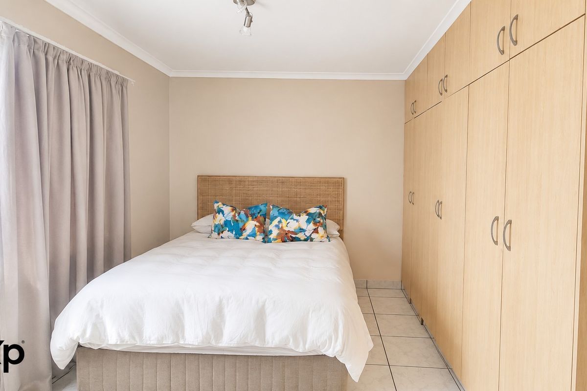 A well-maintained bedroom featuring neutral wall tones, tiled flooring, and extensive floor-to-ceiling built-in wooden cupboards for ample storage.