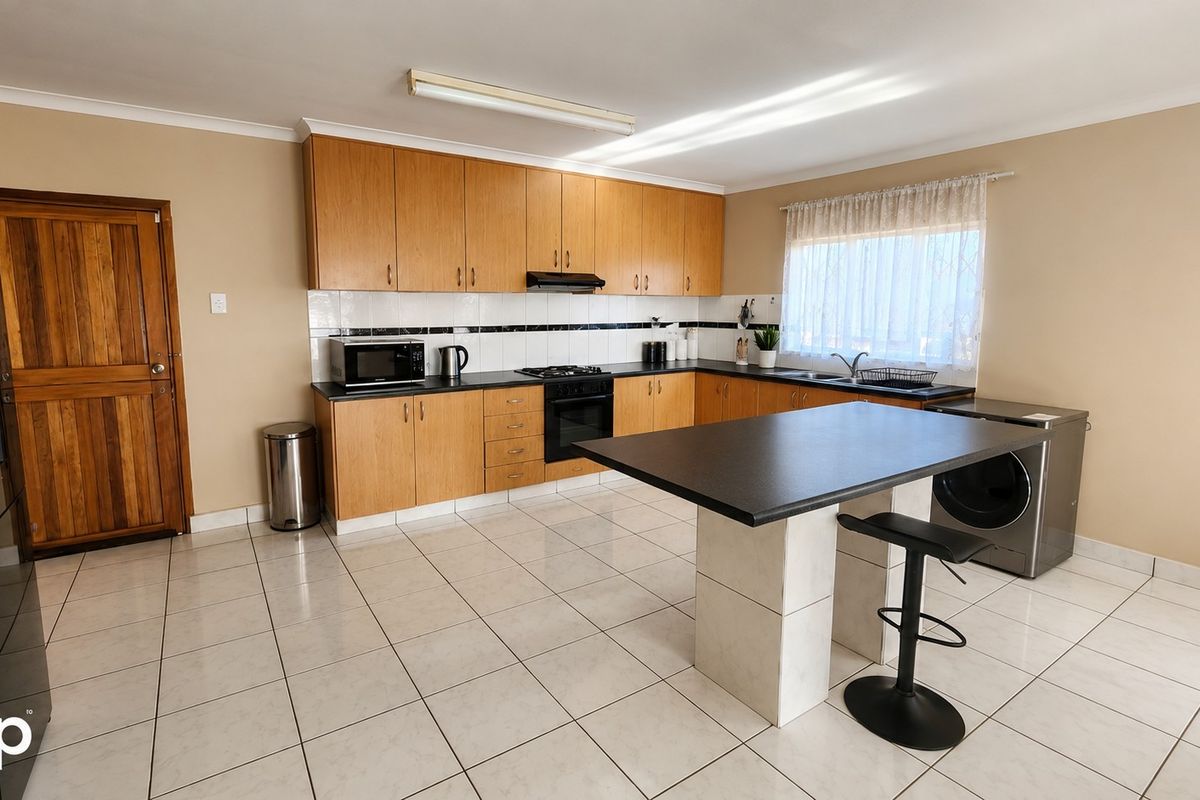 Functional kitchen featuring light wood cabinetry, dark countertops, a central island, tiled flooring, and integrated cooking appliances.