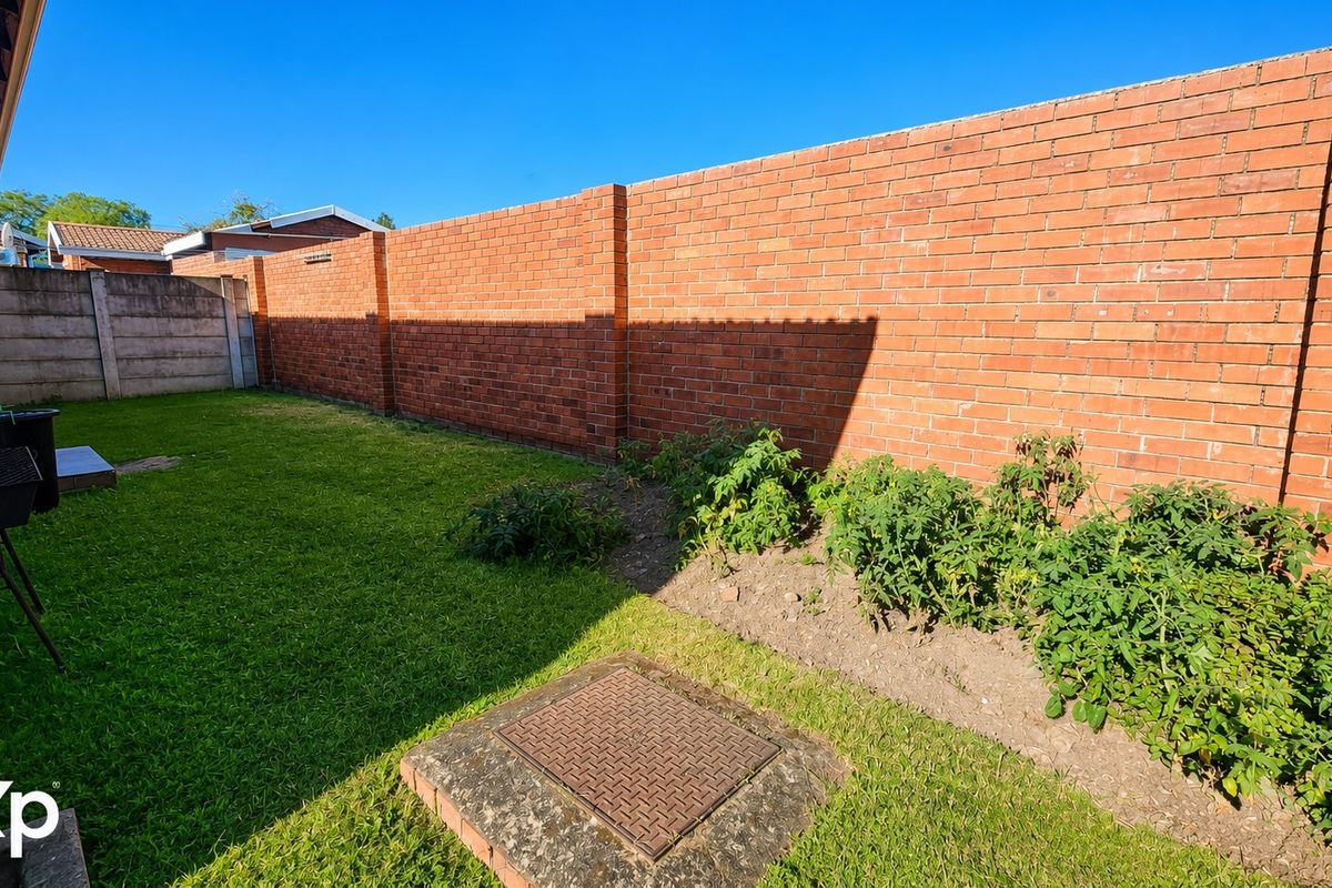 A private rear garden area featuring a well-maintained lawn and a high brick boundary wall for added privacy.
