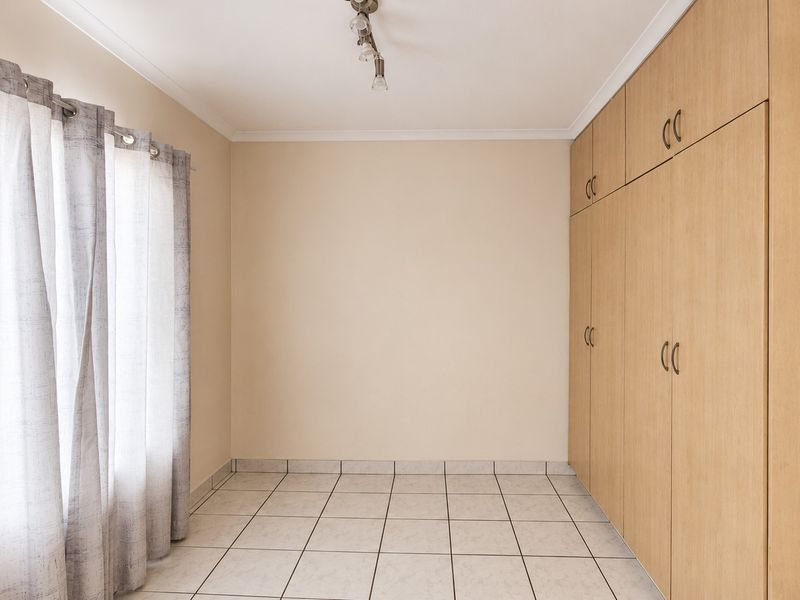 A bright, empty bedroom featuring neutral tiled flooring, built-in wooden cupboards, and a clean, minimalist aesthetic.