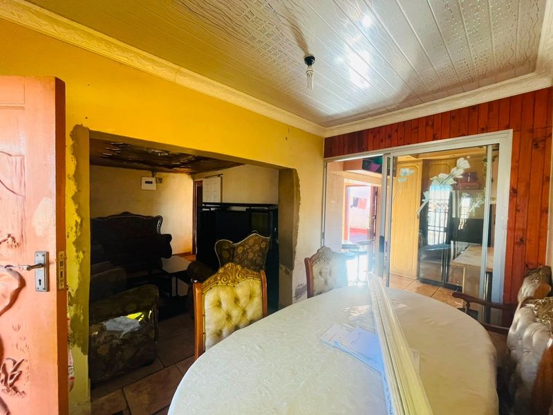 Open plan living and dining area featuring tiled floors, timber wall paneling, and sliding glass doors, requiring cosmetic attention to wall finishes.