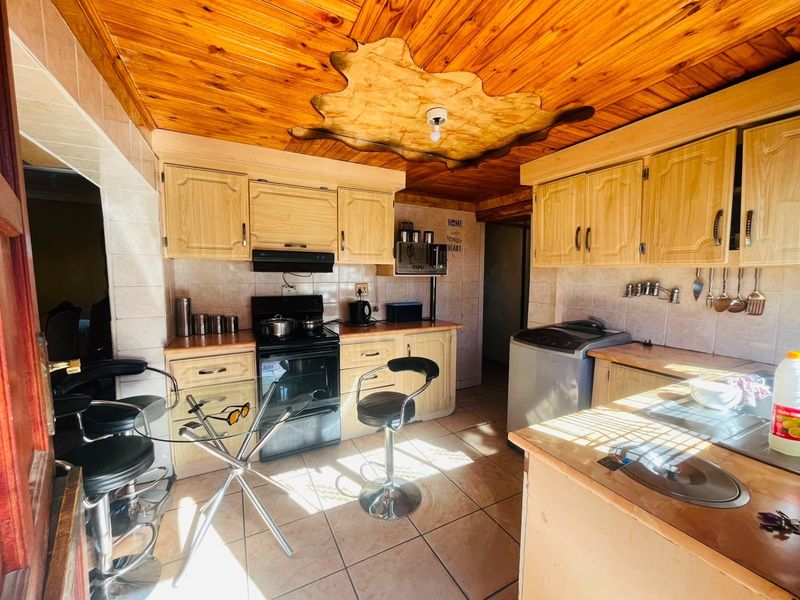 A functional kitchen featuring wooden cabinetry, tiled flooring, and a distinctive wooden tongue and groove ceiling with a central decorative feature.