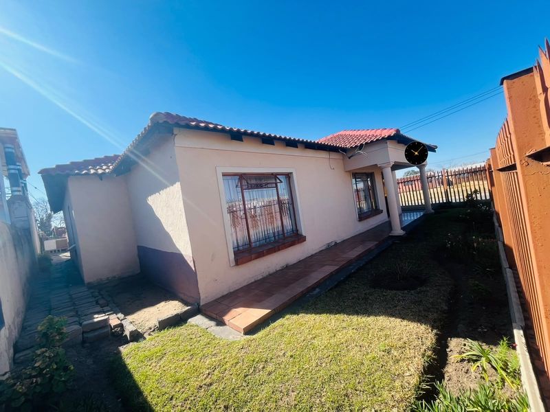 Rear view of the house featuring a tiled roof, covered patio area with concrete columns, and a small garden with paved walkway.