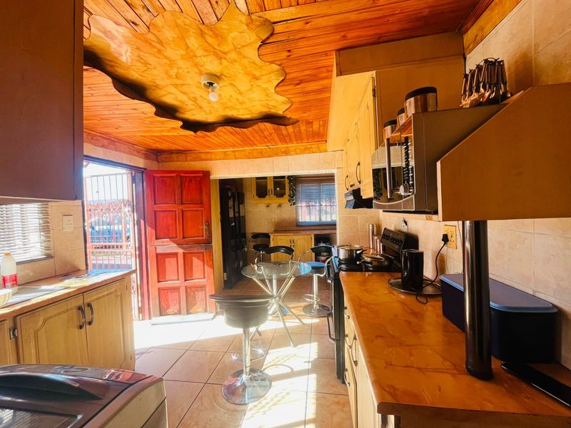 A functional kitchen featuring wooden ceiling paneling, tiled floors, and built-in cabinetry with integrated appliances, offering direct access to the exterior.