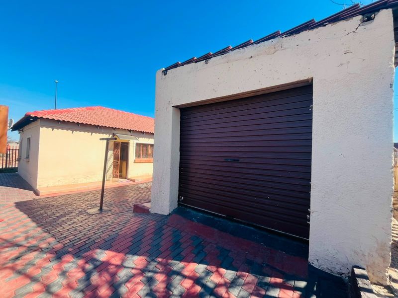 Exterior view of a detached garage featuring a roller shutter door and paved driveway, situated adjacent to the main residential dwelling.