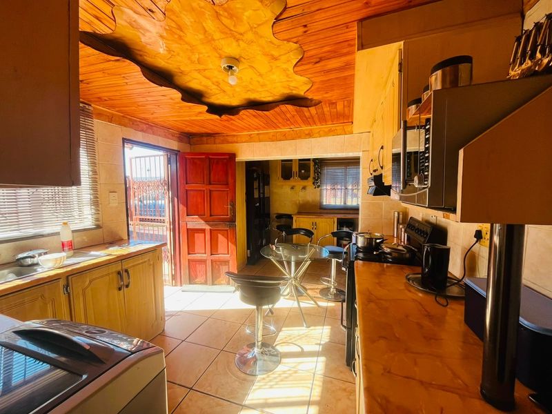 A functional kitchen featuring wooden ceiling paneling, tiled flooring, laminate countertops, and built-in cabinetry with direct access to the exterior.