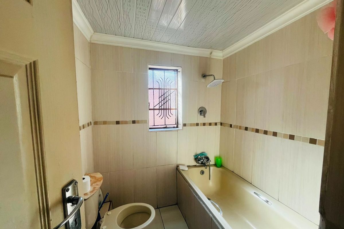 A compact bathroom featuring a bathtub with shower head, toilet, and neutral wall tiling with a decorative border.