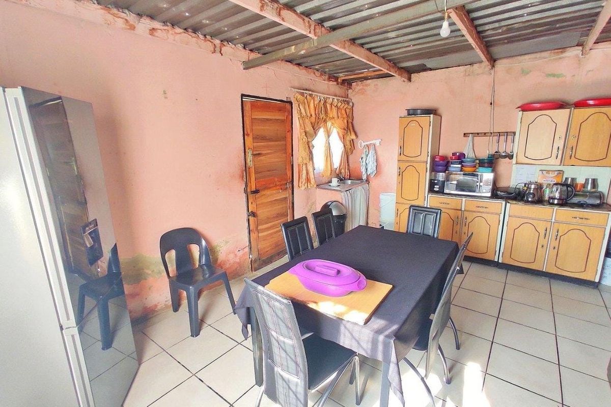 A functional kitchen area featuring tiled floors, built-in cabinetry, and an exposed roof structure, currently showing signs of wear and wall dampness.
