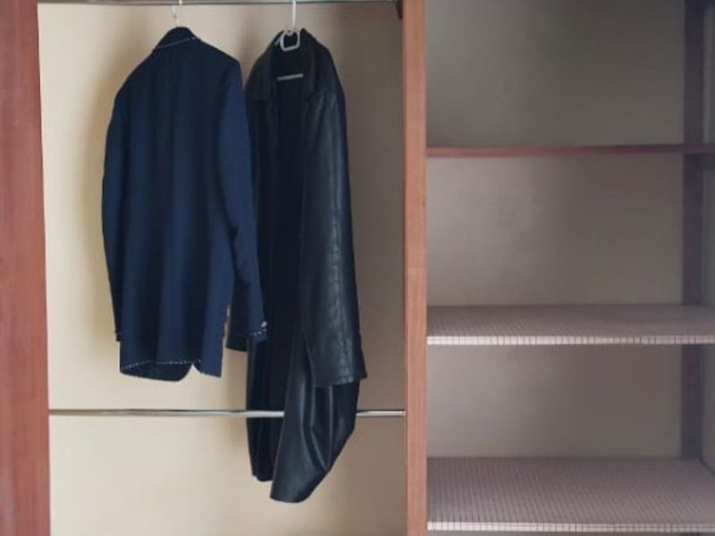 A built-in bedroom wardrobe featuring overhead storage cupboards, hanging rails, and open shelving units.