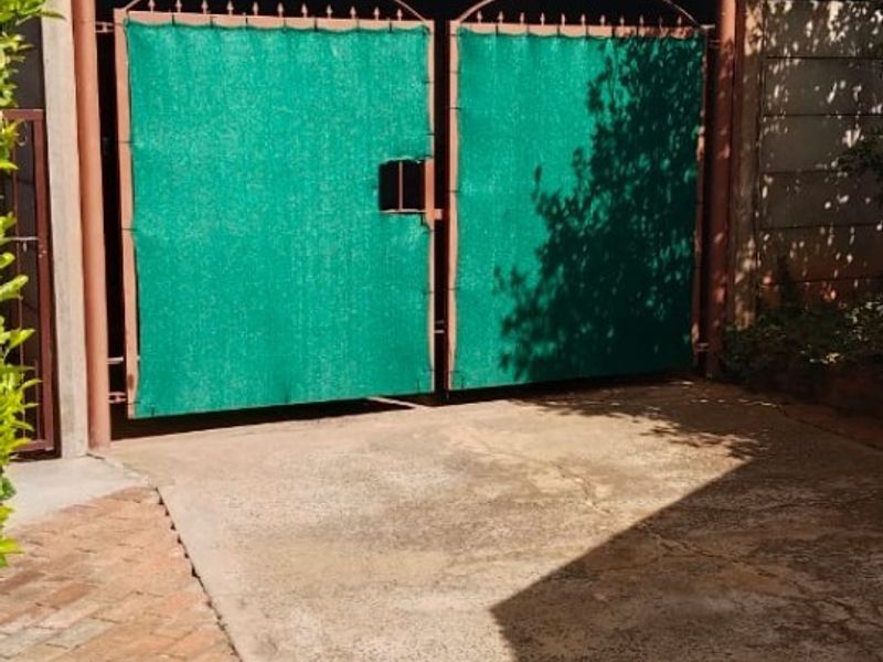 Front entrance area featuring a metal driveway gate with privacy screening, concrete driveway, and brick paved pathway.