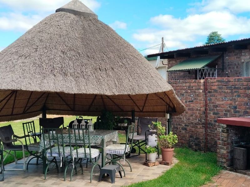 Outdoor entertainment area featuring a traditional thatched lapa roof and a brick built-in braai, set within a garden space.