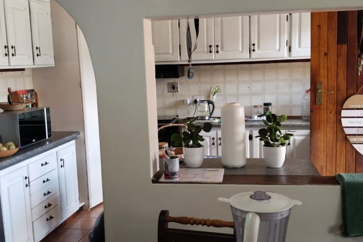 A functional kitchen featuring white cabinetry, tiled backsplash, and a convenient serving hatch opening into the adjacent living area.