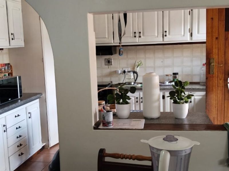 A functional kitchen featuring white cabinetry, tiled backsplash, and a convenient serving hatch opening into the adjacent living area.