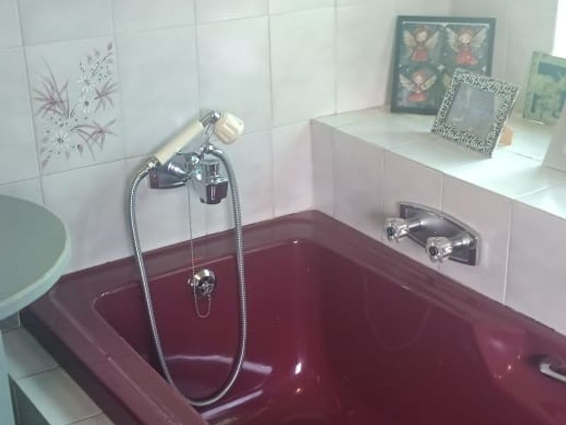 A bathroom featuring a built-in burgundy bathtub with chrome fixtures and decorative ceramic wall tiles.