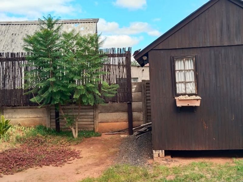 A rear garden area featuring a timber storage shed, enclosed by a precast concrete wall and decorative reed fencing.