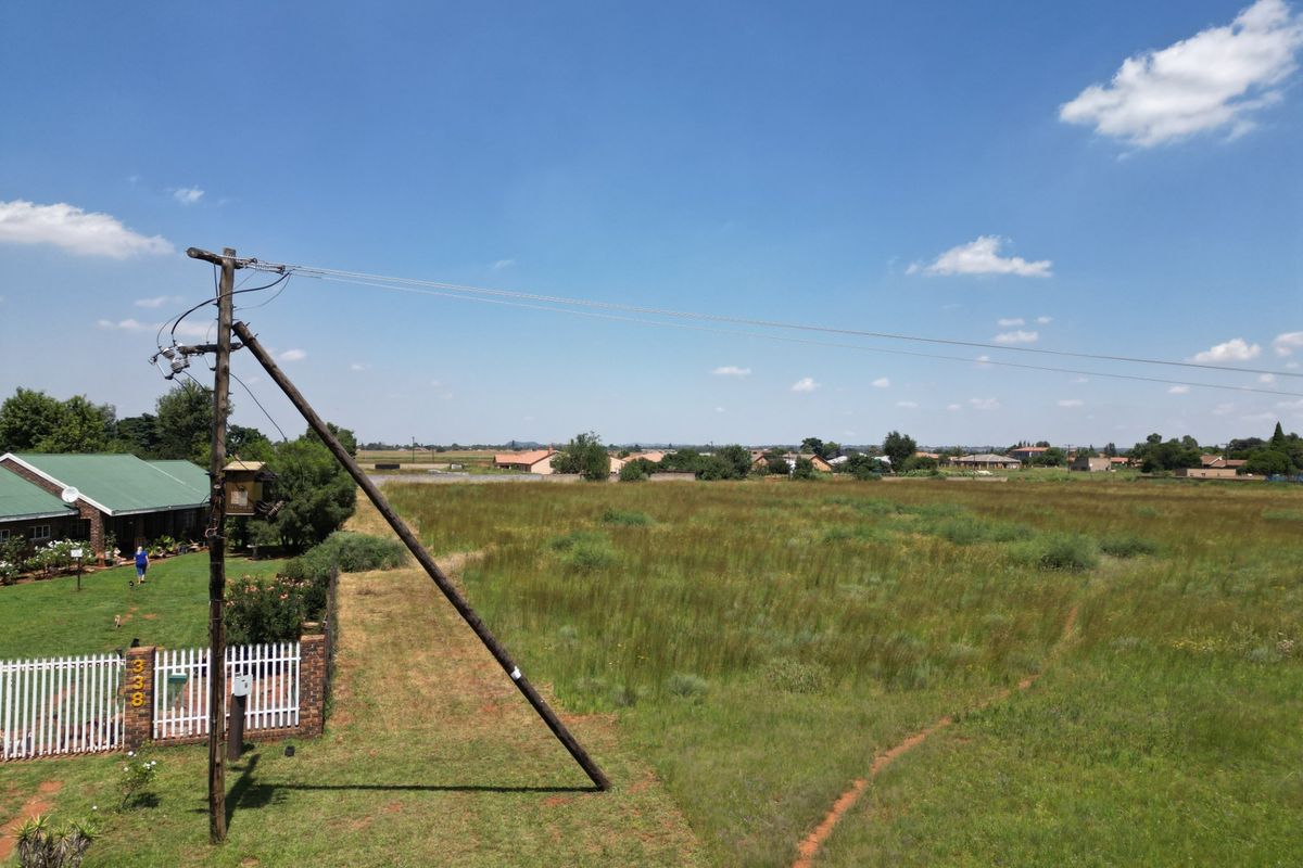 Aerial view of a vacant residential plot featuring open grassland, perimeter fencing, and an existing utility pole with overhead power lines.