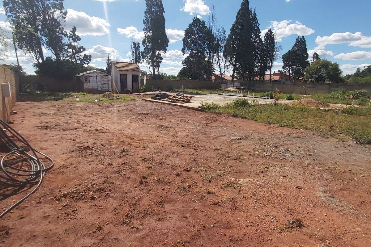 A vacant residential plot featuring a perimeter brick wall, a concrete slab foundation, and a small outbuilding structure.
