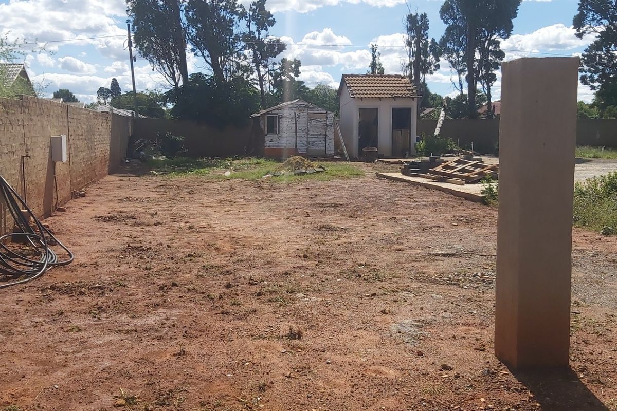 A vacant residential plot featuring a perimeter brick wall, a concrete slab foundation, and an existing outbuilding structure in need of maintenance.