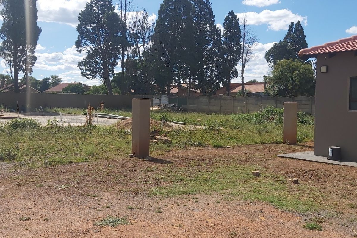 A view of a residential plot featuring a concrete slab, perimeter wall, and an existing structure with a tiled roof.